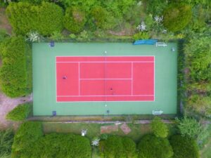 Vue drone d’un court de tennis en béton poreux terminé par ADN-SOL, mettant en valeur la qualité de la surface et l’agencement du terrain.