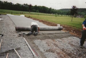 Chef de chantier de l’équipe ADN-SOL en train de lisser une dalle de béton poreux pour la construction d’un terrain de tennis, mettant en avant le processus professionnel et la qualité du matériau.