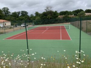 Un court de tennis en béton poreux fraîchement terminé et réceptionné par ADN-SOL, avec des clients satisfaits célébrant la qualité du travail.