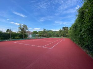 Un court de tennis en béton poreux entièrement rénové par ADN-SOL, avec une surface rouge et des tracés blancs conformes aux réglementations de la Fédération Française de Tennis.