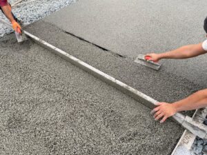 Un chef de chantier ADN-SOL en action, lissant la dalle d’un court de tennis en béton poreux tout en vérifiant les derniers détails avant la finalisation.