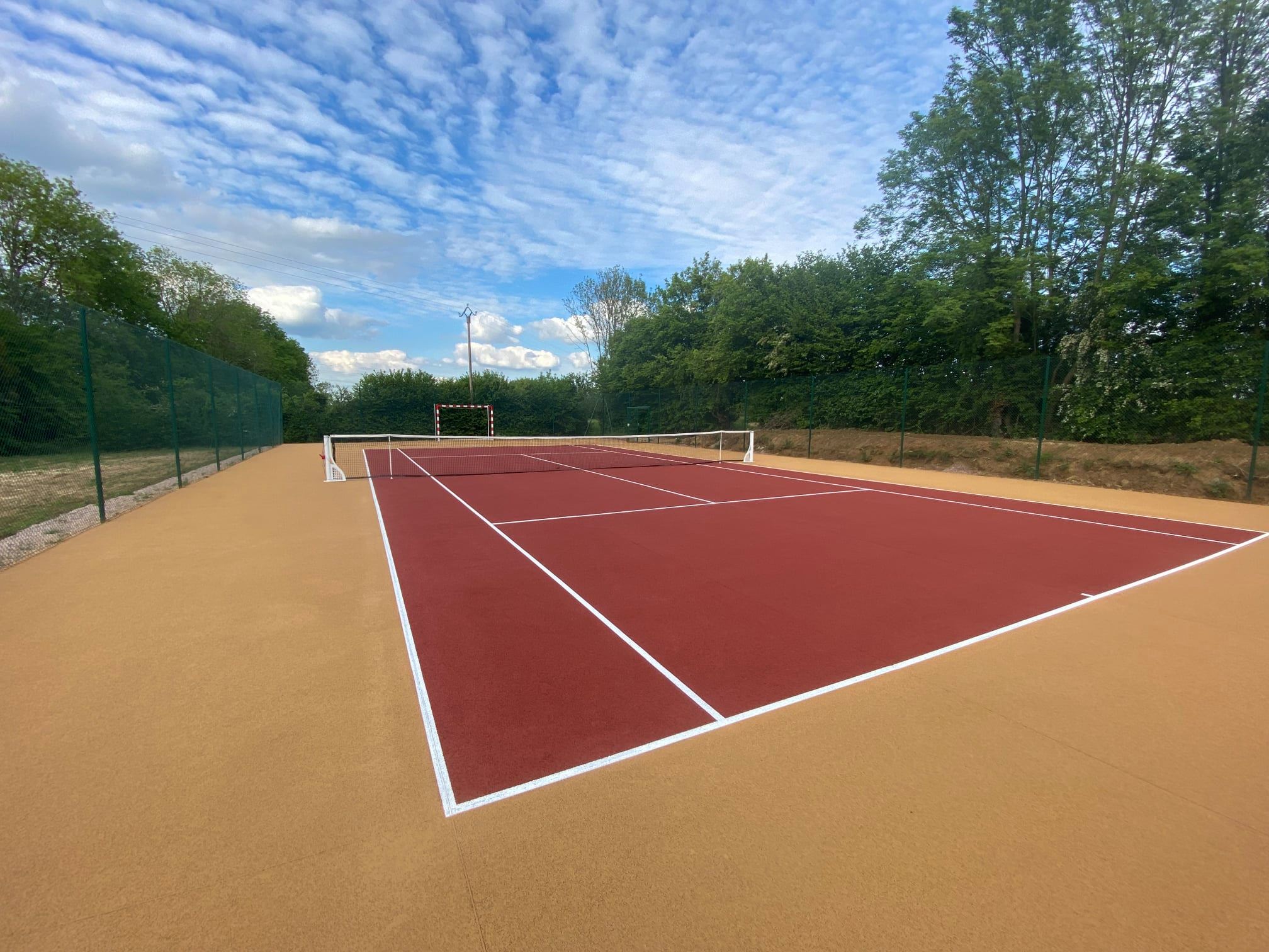 Court de tennis privé en béton poreux beige et rouge : finition durable et drainante